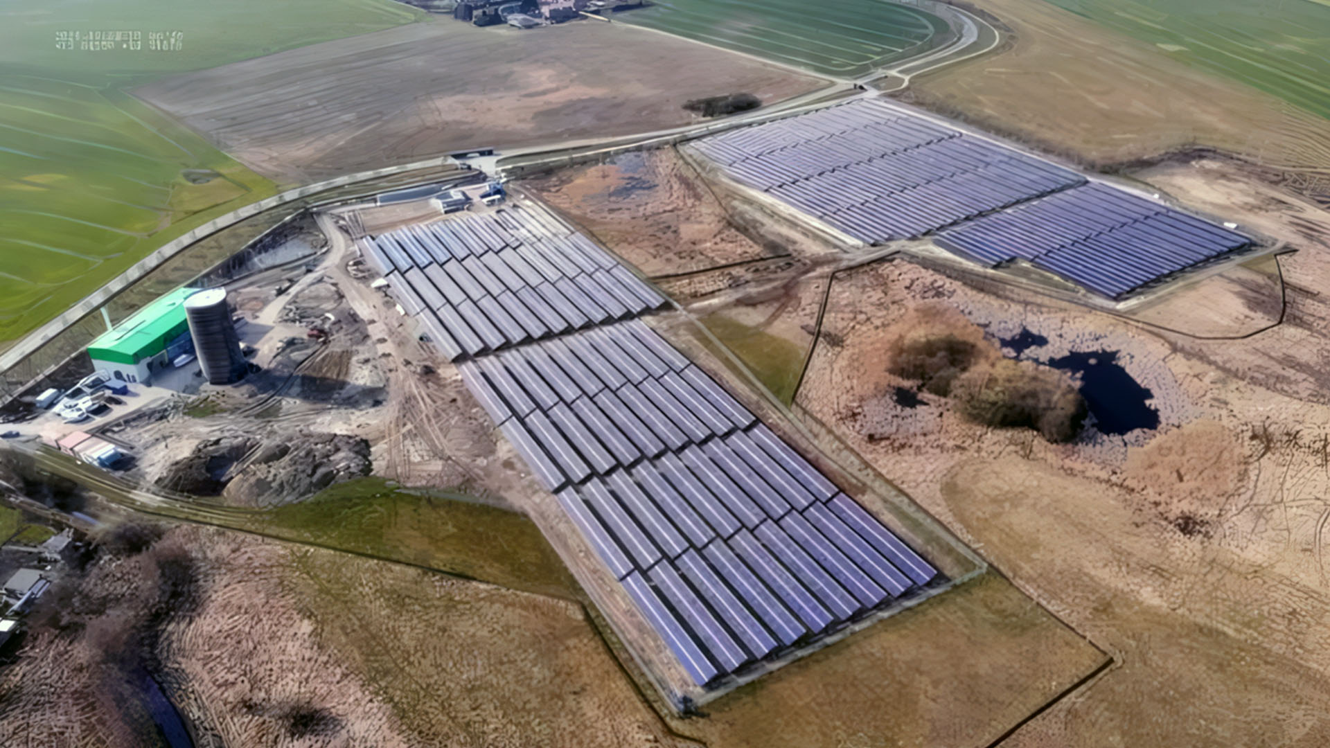 Aerial view of a solar thermal plant with several large collector fields, an operations building and a cylindrical storage tank surrounded by agricultural land.