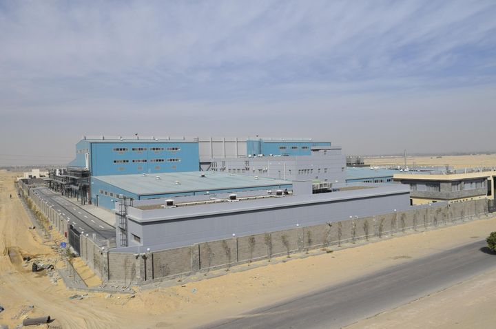 Aerial view of the chemical plant’s blue and grey buildings in a sandy industrial area. A road runs in front of the walled site.